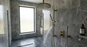 Sophisticated brushed bronze luxury rain shower head fixed to a premium grey marble tiled bathroom wall.