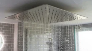 Detail of a brushed nickel ceiling mounted rain shower head neatly installed onto a plastered bathroom ceiling.