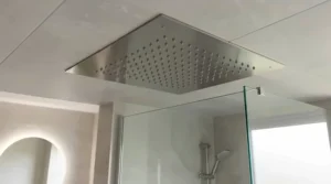 Polished chrome square ceiling mounted rain shower head with rub-clean nozzles installed in a contemporary walk-in shower.