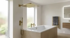 Square rain shower head with a sleek wall-mounted brass arm extension over a bathtub.